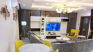Een moderne woonkamer met een bank, gele stoelen, een marmeren tafel en een televisie.