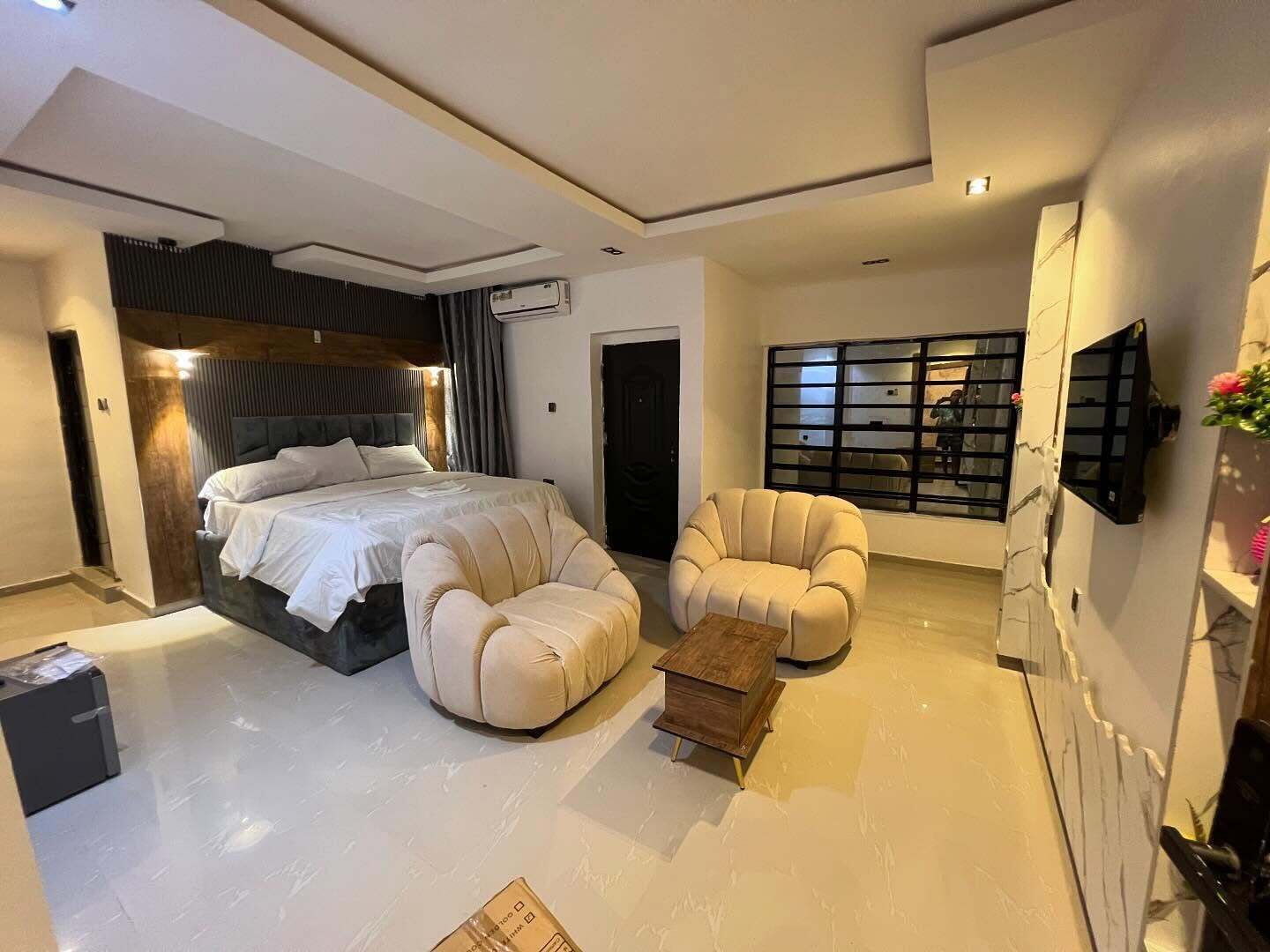 Een moderne slaapkamer met een groot bed, twee fauteuils, een klein houten tafeltje en een aan de muur bevestigde televisie.