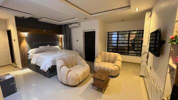 Een moderne slaapkamer met een groot bed, twee fauteuils, een klein houten tafeltje en een aan de muur bevestigde televisie.