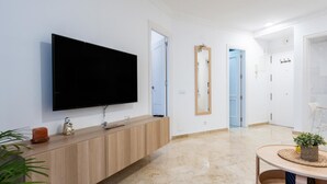 Una sala de estar moderna con un televisor de pantalla plana, una consola de madera, una mesa redonda de centro y un espejo.