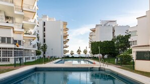 Un hotel moderno con una piscina central, rodeado de edificios blancos y palmeras.