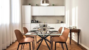 A modern dining area with a glass-top table, brown chairs, and a pendant light. - Ca' delle Contesse   Elegant 2BR apartment in Liberty villa   spectacular view! (Lido)