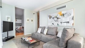 A modern living room with a grey sofa, a coffee table with books, a flat-screen TV, and abstract art on the wall. - Ca' delle Contesse   Elegant 2BR apartment in Liberty villa   spectacular view! (Lido)