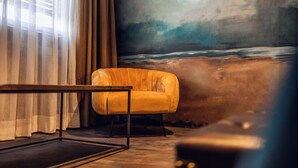 A room with a sofa, a table, and a painting of a beach scene. - Loom Hotel (Bolzano)