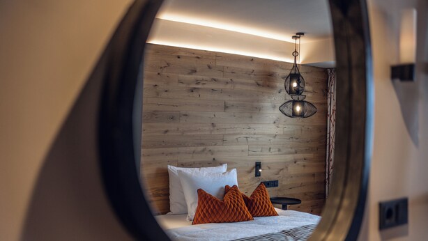 A bedroom with a wooden wall, a bed with white and orange pillows, and a hanging light fixture. - Loom Hotel (Bolzano)
