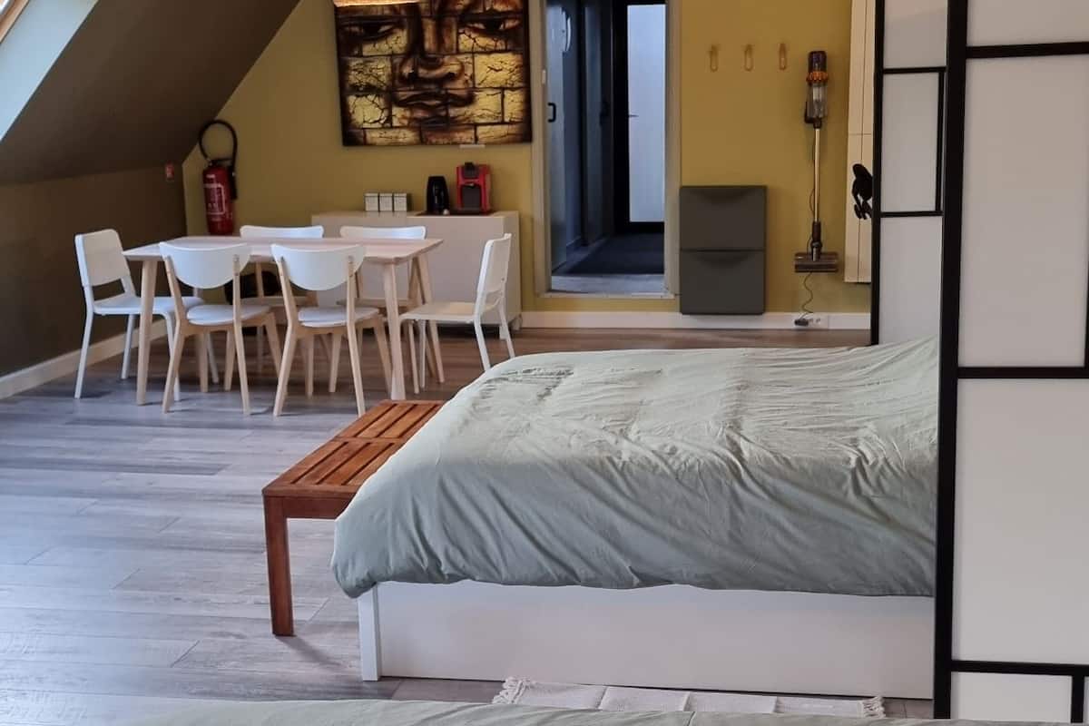 Quarto com cama grande, área de refeições com cadeiras, pintura na parede e luminária no teto.