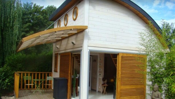 A modern house with a curved roof, a wooden deck, and a glass door leading to an interior space. - LA GRANGE AU CORPS (Gussignies)