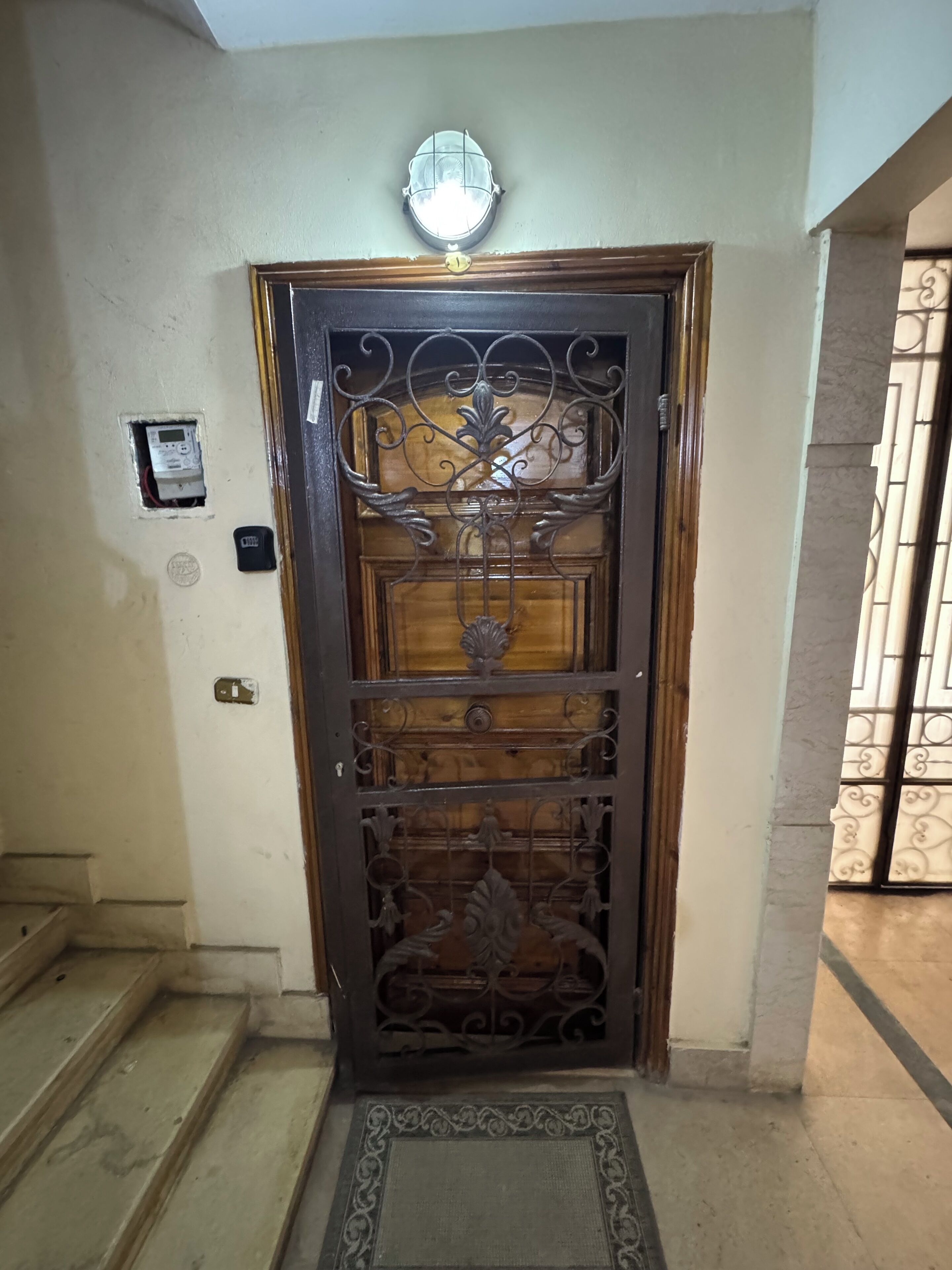 Una porta de fusta amb detalls metàl·lics decoratius, una làmpada penjant a sobre i un felp a la part frontal.