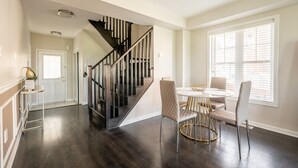 A modern interior with a dark wood staircase, a dining area with round tables and cushioned chairs, and a large window with blinds. - GLOBALSTAY. Modern 3 Bedroom House in Brampton. BBQ, parking. (Brampton/Canada)