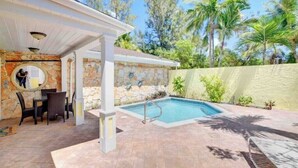 A covered outdoor area with a swimming pool, stone walls, and a patio with chairs and a table. - Seaclusion - Private Pool near Atlantis+Beach (Paradise Island)