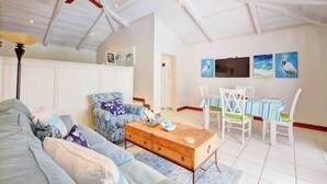 A spacious room with a high ceiling, a ceiling fan, a wooden coffee table, a sofa, a patterned armchair, a dining table with chairs, and wall art. - Seaclusion - Private Pool near Atlantis+Beach (Paradise Island)