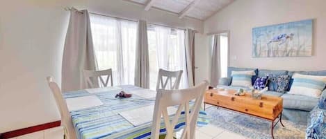 A dining area with a table set for two, a wooden coffee table, and a sofa in the background.