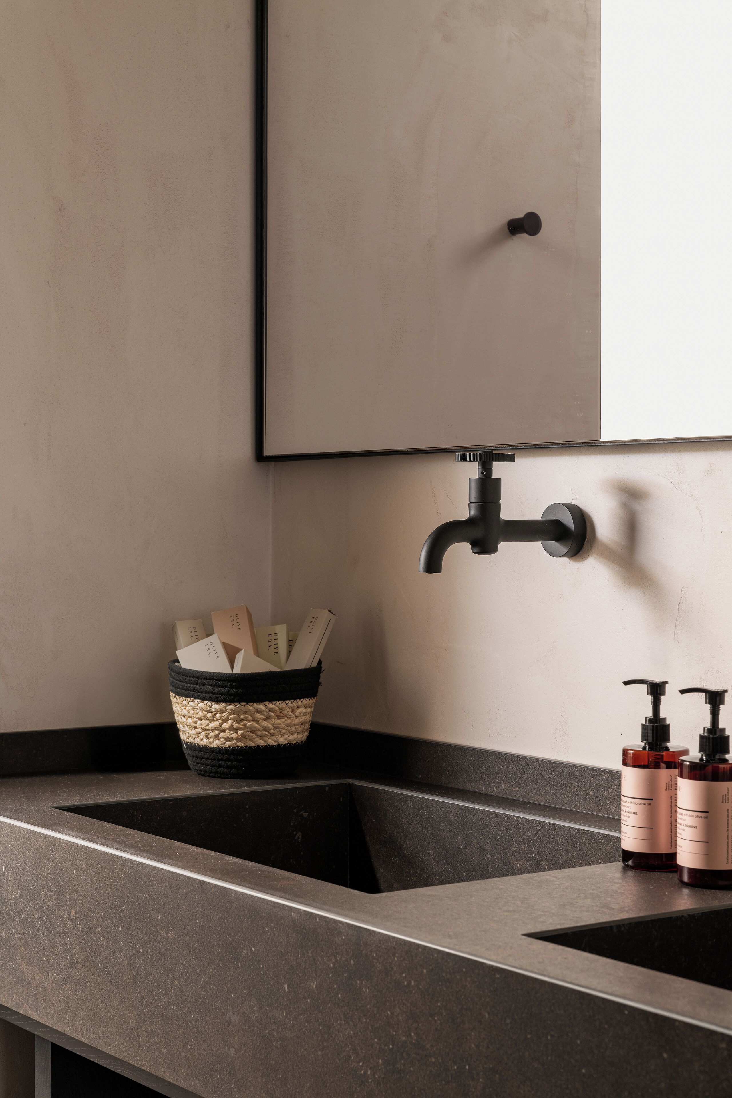 Ein Badezimmer mit zwei Waschbecken, einem schwarzen Wasserhahn, einem gewebten Korb mit Büchern und zwei Seifenflaschen.