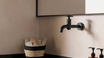 Ein Badezimmer mit zwei Waschbecken, einem schwarzen Wasserhahn, einem gewebten Korb mit Büchern und zwei Seifenflaschen.