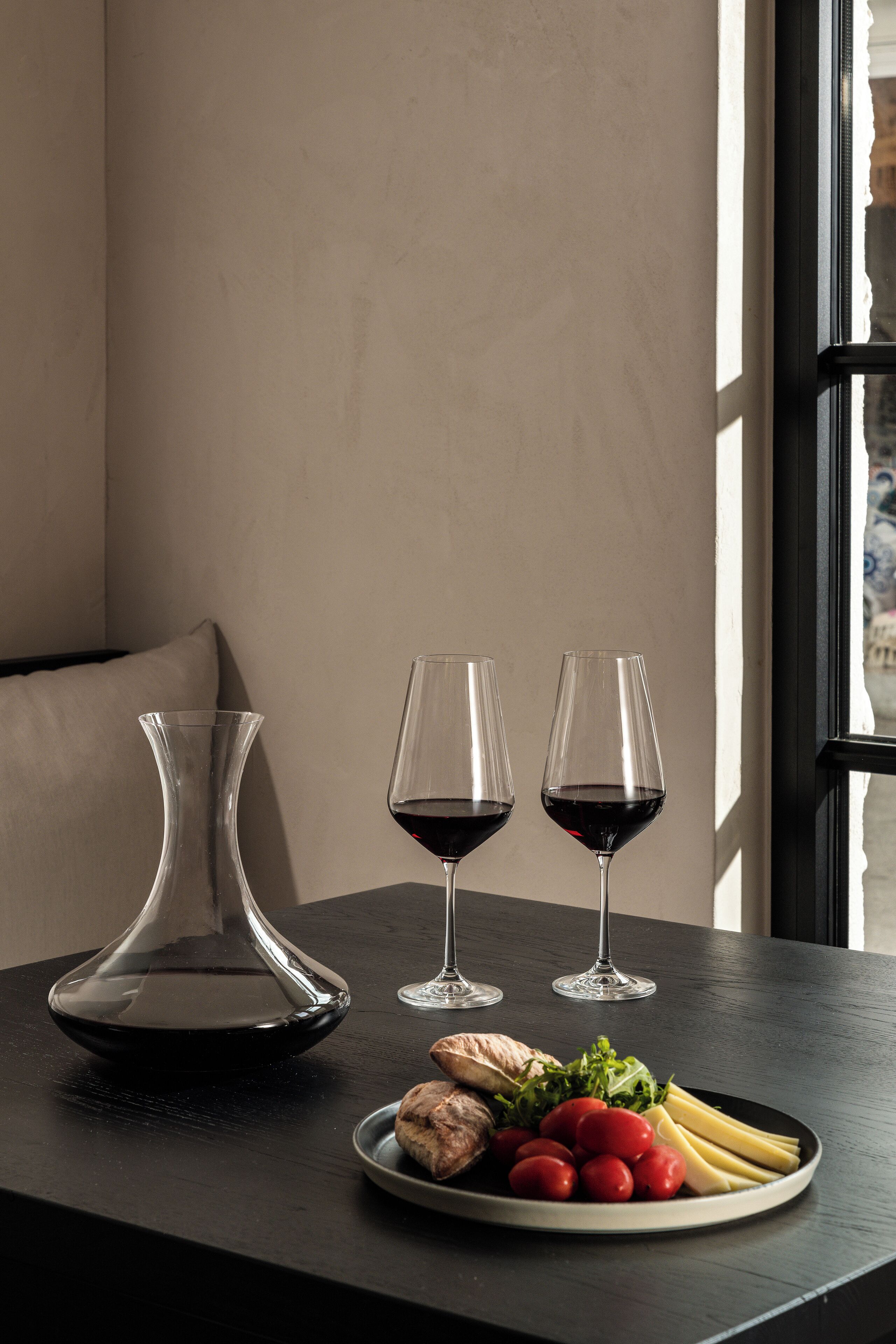 A table with a plate of food, two wine glasses, and a vase.