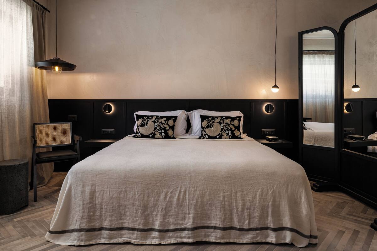 Una habitación de hotel con una cama grande, dos mesitas de noche, un espejo y una lámpara colgante.