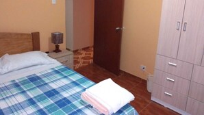 A bedroom with a bed, a nightstand, a lamp, a wardrobe, and a door.