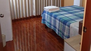 A small, tidy room with a bed, a wooden floor, and a window with curtains.