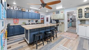 Una cocina moderna con armarios azules, una isla de madera con taburetes, un ventilador de techo y un refrigerador al fondo.