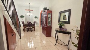 A hallway with a dining area, a ceiling fan, a cabinet, and a table with a sign.