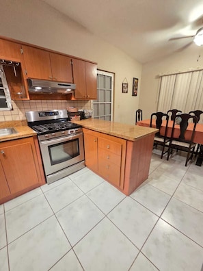 Una cocina con armarios de madera, estufa de acero inoxidable y piso de baldosas.