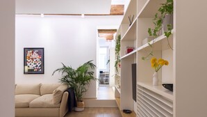 A modern living room with a beige sofa, a large potted plant, and a white shelving unit with decorative items.