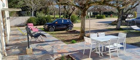 A patio with outdoor furniture, a car parked nearby, and a tree in the background.
