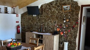 A cozy kitchen with a stone wall, wooden ceiling, and a dining area with chairs and a table.