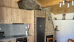 A kitchen with wooden cabinets, a stone wall, a built-in oven, and a black refrigerator.