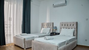 Habitación de hotel con dos camas, una mesita de noche con lámpara y un equipo de aire acondicionado en la pared.