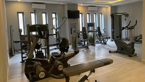 A gym with various exercise machines, a bench, and large windows allowing natural light. - Sound View Lounge and Apartments (Enugu)