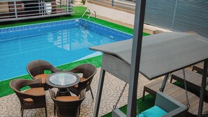 A swimming pool with a tiled edge, surrounded by wicker furniture and a glass table. - Sound View Lounge and Apartments (Enugu)