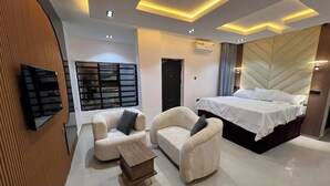 A modern bedroom with a large bed, two armchairs, a small wooden table, and a TV mounted on the wall. - Sound View Lounge and Apartments (Enugu)