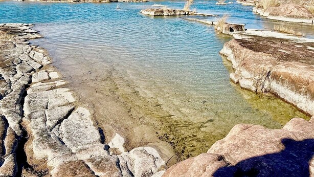 Un río cristalino con orillas rocosas y vegetación escasa.