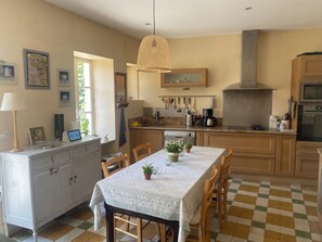 A kitchen with wooden cabinets, a dining table with chairs, a hanging light fixture, and a window with a view.