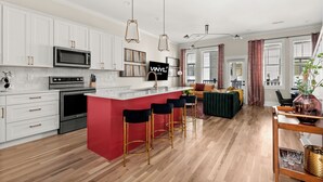 Une cuisine moderne avec des meubles blancs, un îlot central rouge et des tabourets de bar noirs.