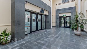 A modern building entrance with glass doors, a security camera, and a sign indicating a public area. - 10 Mansion House - Indoor Pool Sea Views Gym (Tenby)