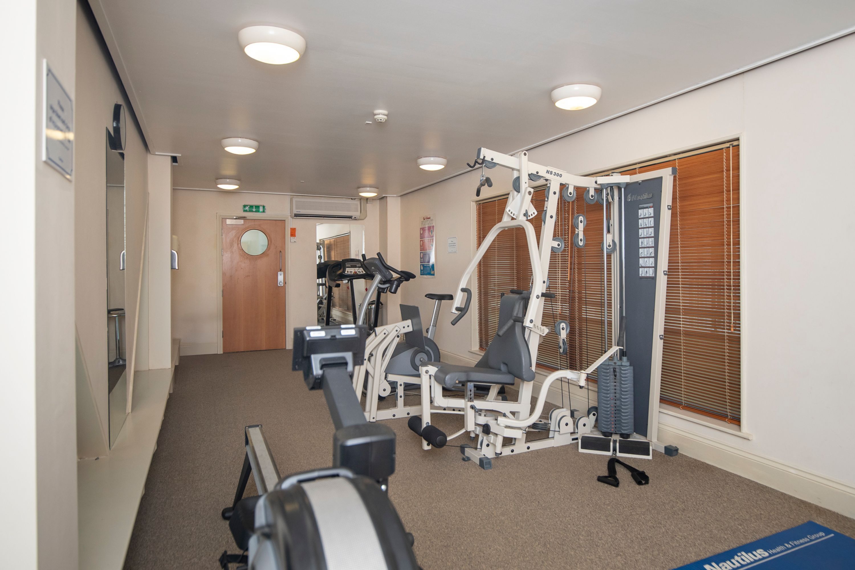 A gym with exercise equipment, a door, and a window with blinds.