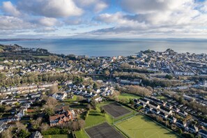 An aerial view of a coastal town with residential areas, a sports field, and a large body of water in the background. - Little Rosemount - Close to Town Beach and Shops (Tenby)