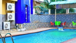 A swimming pool with a tiled deck, air conditioning units, and colorful chairs. - Nafelis Hotel Enugu (Enugu)