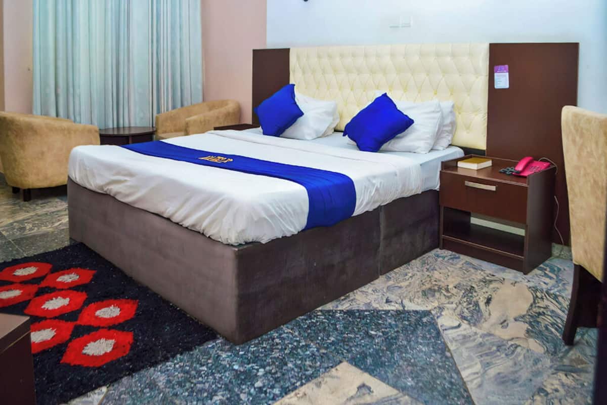 Hotellihuone, jossa on suuri sänky, yöpöytä, tuoli ja punavalkokuvioinen matto.