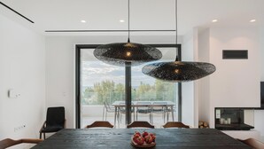 Un comedor moderno con una mesa de madera oscura, dos lámparas colgantes negras y un frutero.