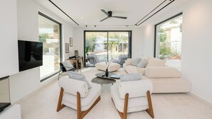 Una sala de estar moderna con televisor de pantalla plana, dos sillones, un sofá, una mesa de centro y un ventilador de techo.