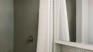 A bathroom with a tiled floor and walls, a shower door, and a mirror.