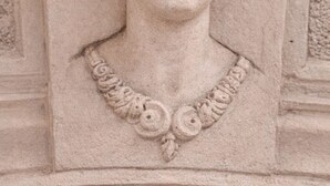 A detailed stone carving of a figure with wings and a headdress, likely part of a building's architecture.