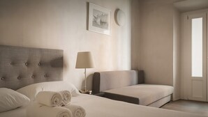 A hotel room with a large bed, a smaller sofa, a bedside lamp, and a framed picture on the wall.
