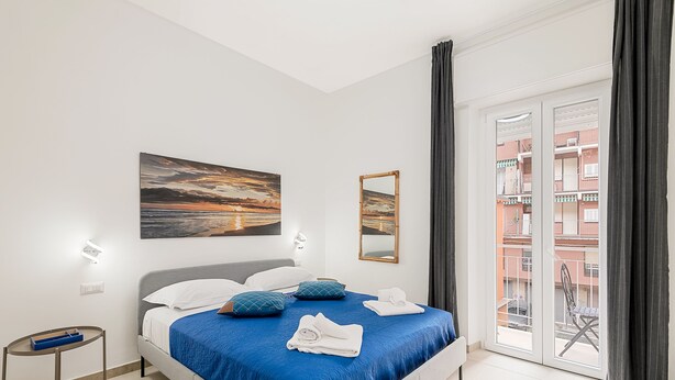 Ein modernes Schlafzimmer mit einem großen Bett, einem Nachttisch, einem Gemälde, einem Spiegel und Blick auf den Balkon.