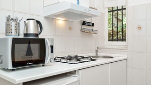 A kitchen with a microwave, kettle, gas stove, and a window with a view of greenery. - Cosy Corner Apartment with Terrace (Monterosso al Mare)