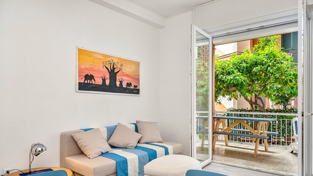 A modern living room with a sofa, a table, and a painting of a sunset scene. - Cosy Corner Apartment with Terrace (Monterosso al Mare)
