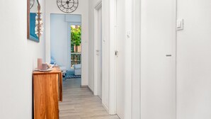 A hallway with a wooden side table, a clock, and a door leading to a room with a blue door and a plant. - Cosy Corner Apartment with Terrace (Monterosso al Mare)